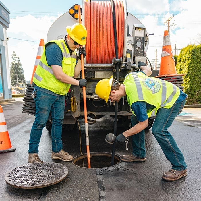 two workers standing behind a truck inspecting a sewer drain