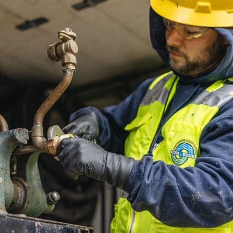 a worker in a hard hat and protective vest using a wrench on a metal device